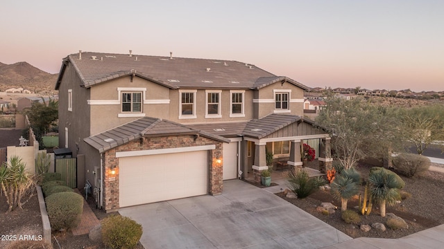 view of front of house with stone siding, concrete driveway, a tile roof, and stucco siding