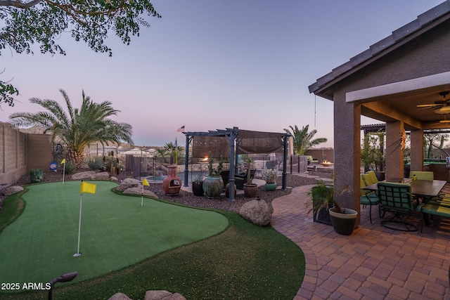 yard at dusk featuring a patio area, a fenced backyard, ceiling fan, and a pergola