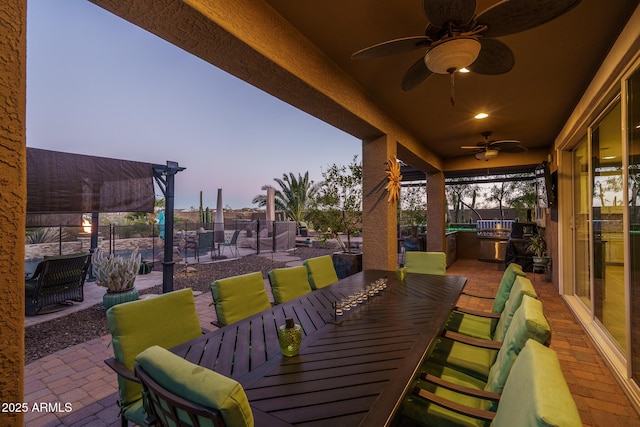 patio terrace at dusk with fence, a ceiling fan, and outdoor dining space