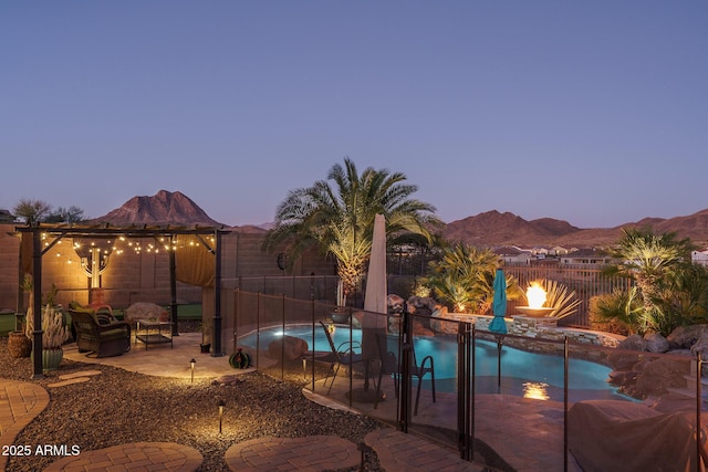 pool at dusk with a fenced in pool, a patio area, a mountain view, a fenced backyard, and a fire pit