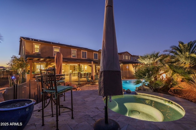 pool at dusk featuring a patio, fence, and a pool with connected hot tub