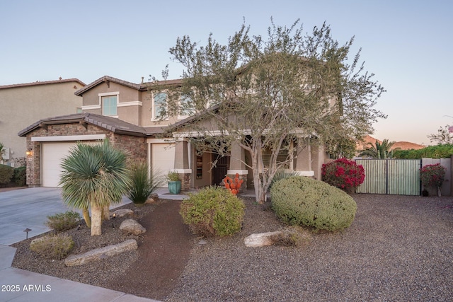 view of front of house with concrete driveway, stone siding, a tiled roof, fence, and stucco siding