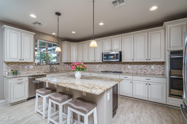 kitchen with light wood finished floors, a kitchen island, visible vents, and stainless steel appliances