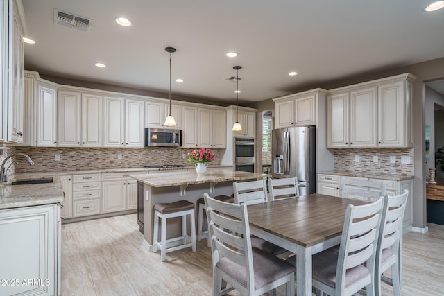 kitchen featuring visible vents, a kitchen island, appliances with stainless steel finishes, light stone countertops, and a sink