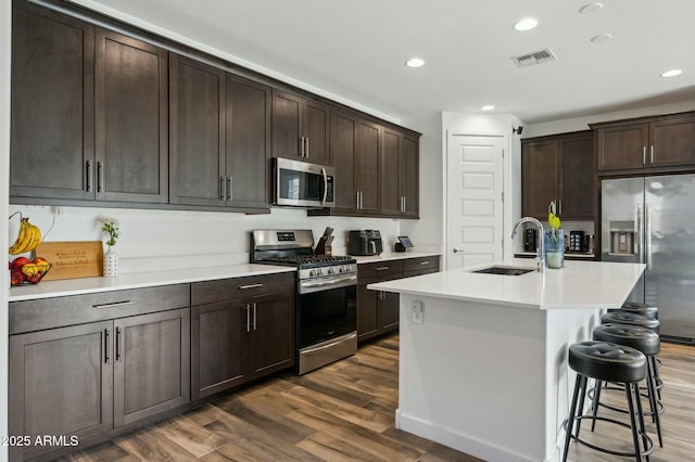 kitchen featuring dark wood-type flooring, a sink, visible vents, dark brown cabinets, and appliances with stainless steel finishes