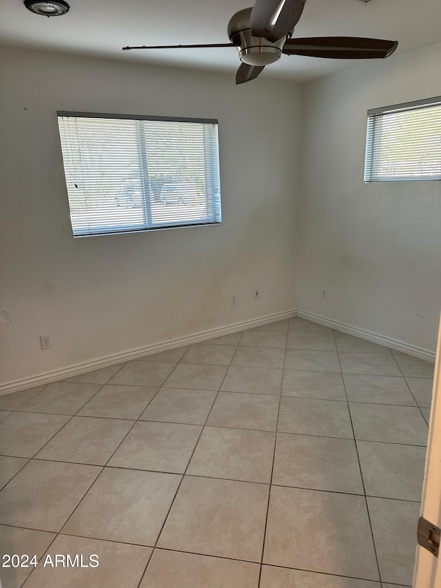 spare room with ceiling fan, a wealth of natural light, and light tile patterned flooring