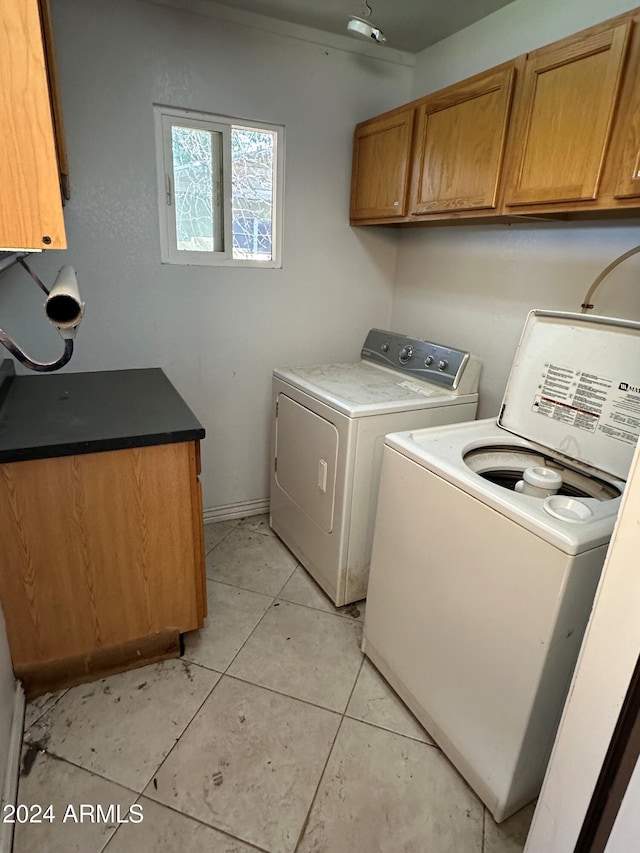 clothes washing area featuring cabinets, light tile patterned floors, and washing machine and clothes dryer