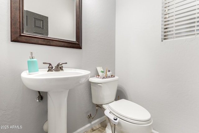 bathroom featuring toilet, a sink, baseboards, and a textured wall