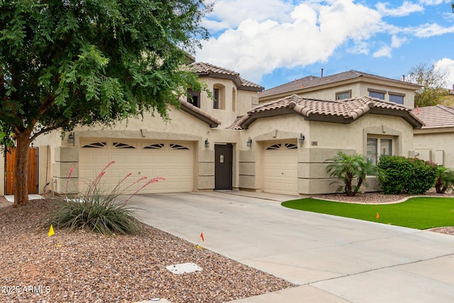 mediterranean / spanish house featuring a tiled roof, stucco siding, driveway, an attached garage, and fence
