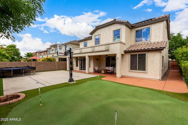 back of house featuring a putting area, a tile roof, a patio, a fenced backyard, and a trampoline