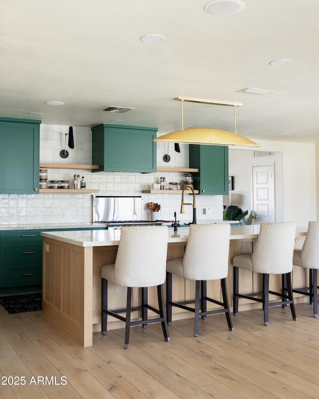 kitchen with light wood finished floors, green cabinetry, a kitchen breakfast bar, open shelves, and backsplash