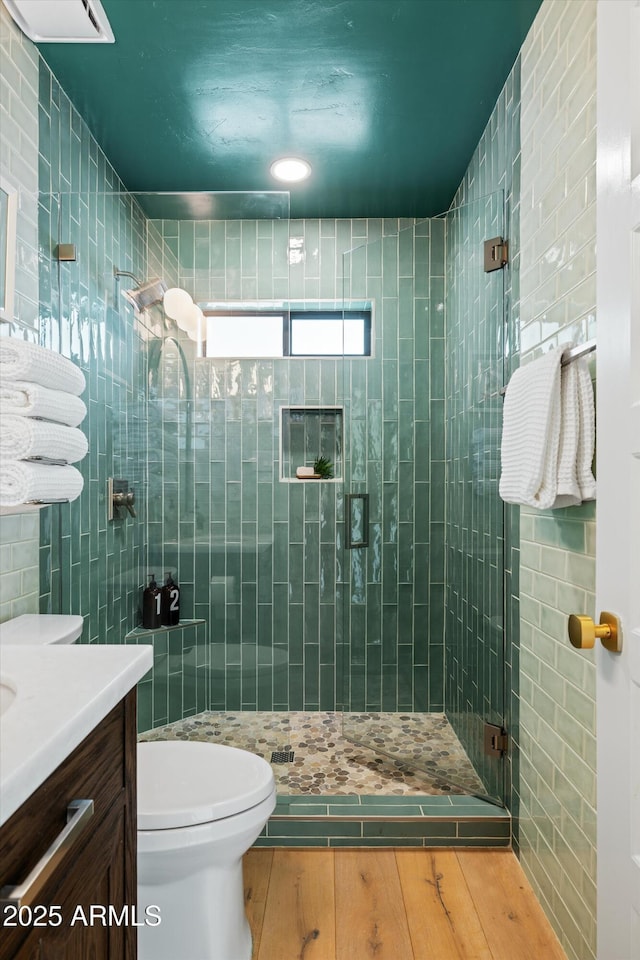 bathroom featuring toilet, wood finished floors, vanity, tile walls, and a shower stall