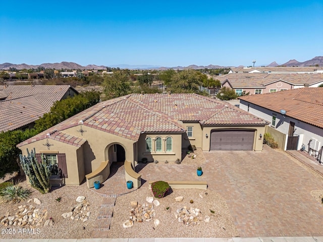 mediterranean / spanish-style home with a tile roof, an attached garage, decorative driveway, a mountain view, and stucco siding