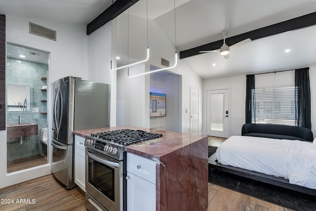 kitchen with white cabinets, hardwood / wood-style floors, appliances with stainless steel finishes, ceiling fan, and vaulted ceiling with beams