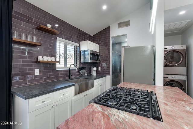 kitchen featuring white cabinetry, stacked washer / dryer, vaulted ceiling, sink, and appliances with stainless steel finishes