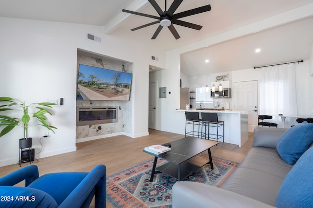 living room with ceiling fan, a high end fireplace, light wood-type flooring, and lofted ceiling with beams