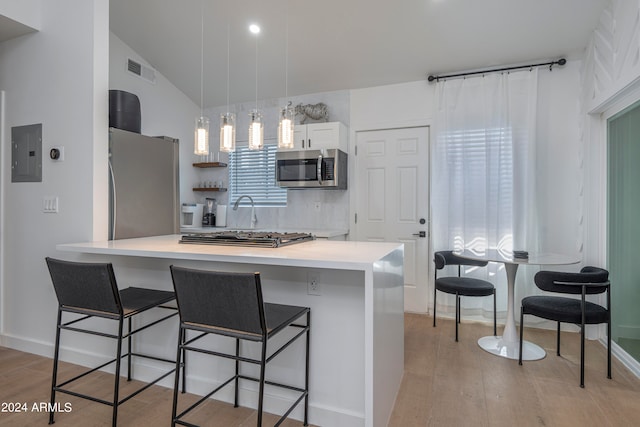 kitchen with light wood-type flooring, appliances with stainless steel finishes, vaulted ceiling, and a breakfast bar area