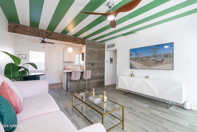 living room featuring beamed ceiling, light hardwood / wood-style flooring, wood walls, and ceiling fan