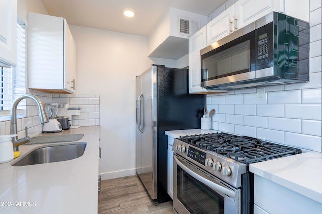 kitchen with white cabinets, backsplash, stainless steel appliances, light hardwood / wood-style floors, and sink