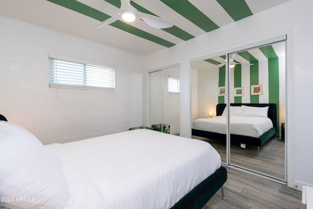 bedroom featuring brick wall, ceiling fan, multiple closets, and hardwood / wood-style flooring