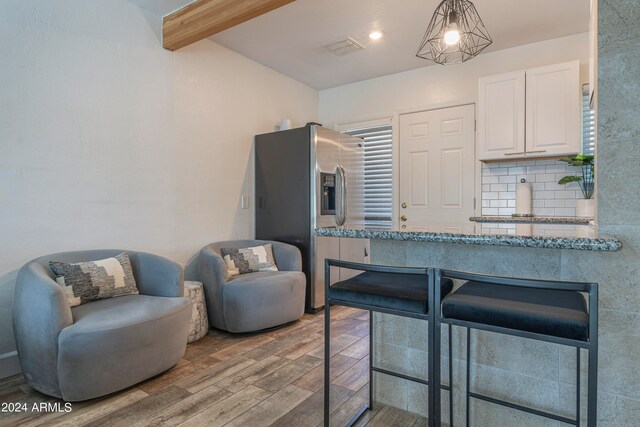 kitchen with stainless steel refrigerator with ice dispenser, beam ceiling, hanging light fixtures, white cabinetry, and light wood-type flooring