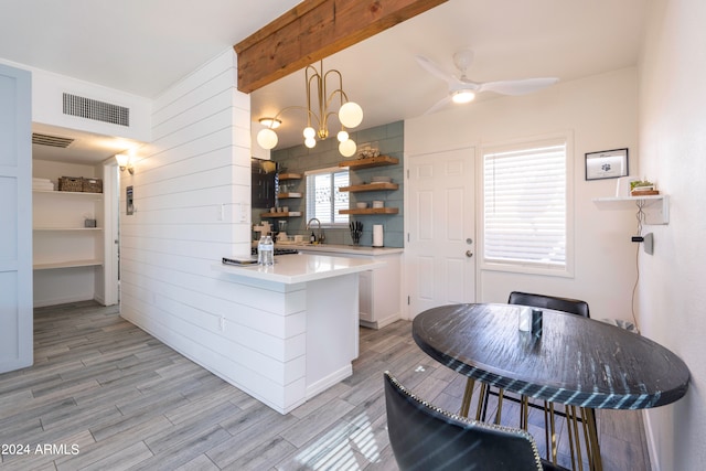 kitchen with light wood-type flooring, ceiling fan with notable chandelier, white cabinetry, kitchen peninsula, and hanging light fixtures