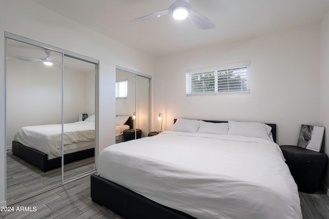 bedroom with light hardwood / wood-style flooring, ceiling fan, and two closets