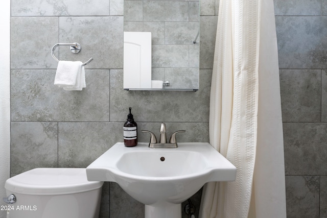 bathroom with tile walls, toilet, a shower with shower curtain, and sink