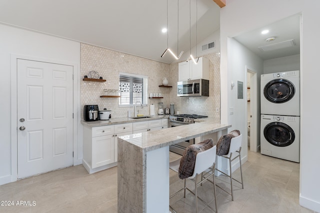 kitchen with white cabinets, stainless steel appliances, sink, stacked washer and dryer, and a breakfast bar area