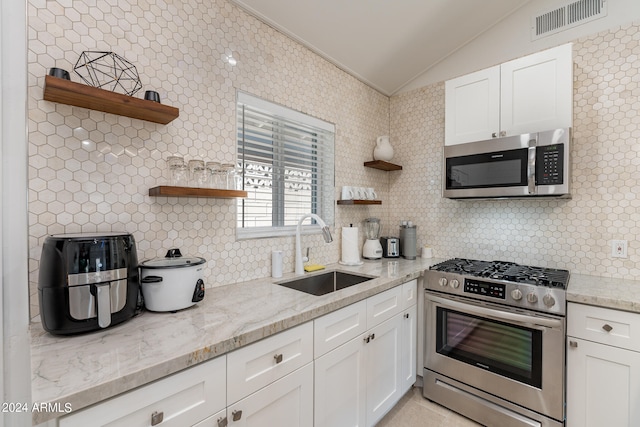 kitchen with appliances with stainless steel finishes, vaulted ceiling, white cabinetry, and sink