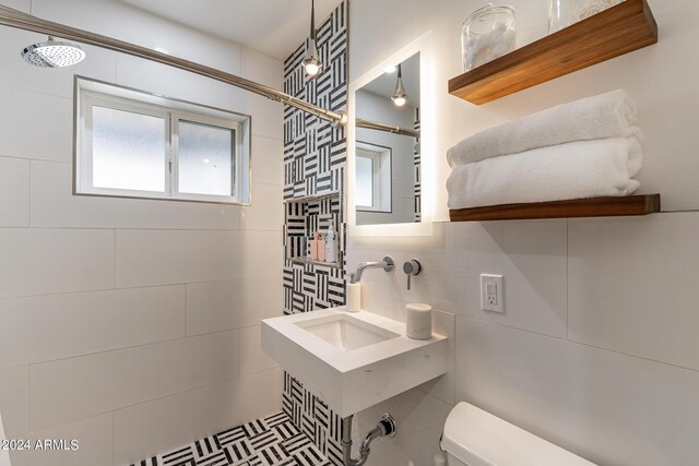 bathroom featuring tile walls, toilet, sink, and tiled shower