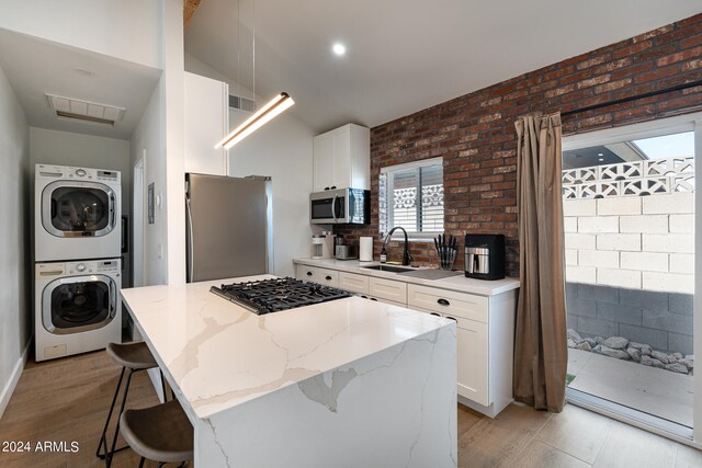 kitchen with appliances with stainless steel finishes, a kitchen island, a breakfast bar, and stacked washer / drying machine