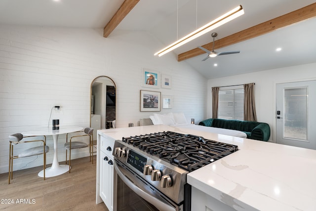 kitchen with stainless steel gas stove, white cabinetry, light stone counters, vaulted ceiling with beams, and light hardwood / wood-style floors