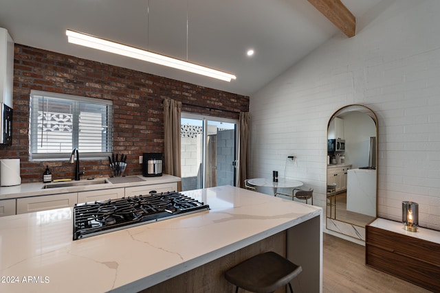 kitchen featuring brick wall, a wealth of natural light, light stone counters, and vaulted ceiling with beams