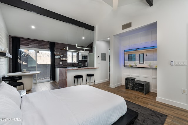 bedroom with beamed ceiling, stainless steel fridge, wood-type flooring, sink, and brick wall