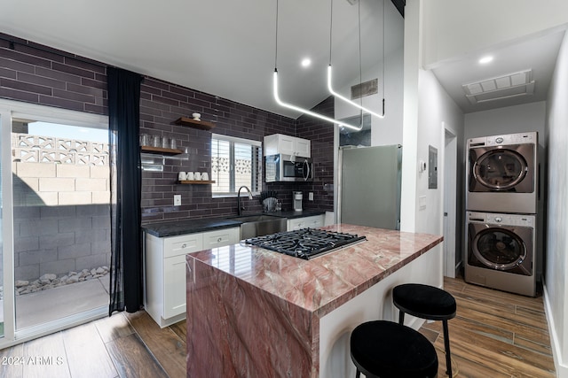 kitchen featuring dark hardwood / wood-style flooring, stacked washing maching and dryer, stainless steel appliances, sink, and white cabinetry