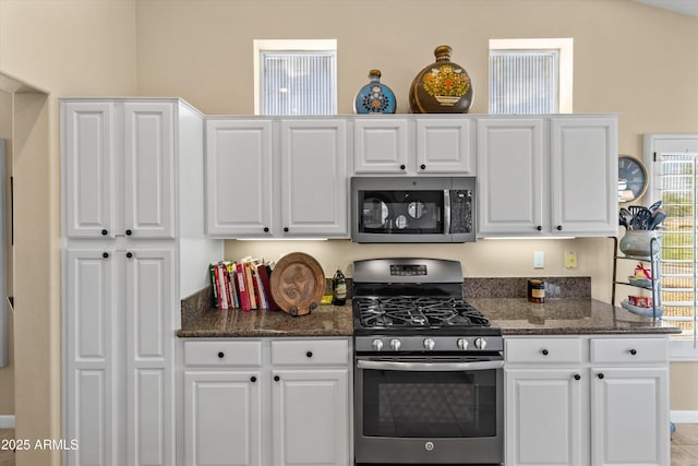 kitchen featuring appliances with stainless steel finishes, dark stone countertops, and white cabinetry