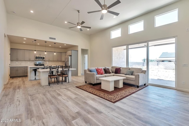 living room with ceiling fan, light hardwood / wood-style floors, and a high ceiling