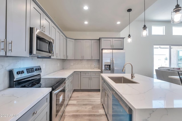 kitchen with light stone countertops, appliances with stainless steel finishes, decorative light fixtures, and sink