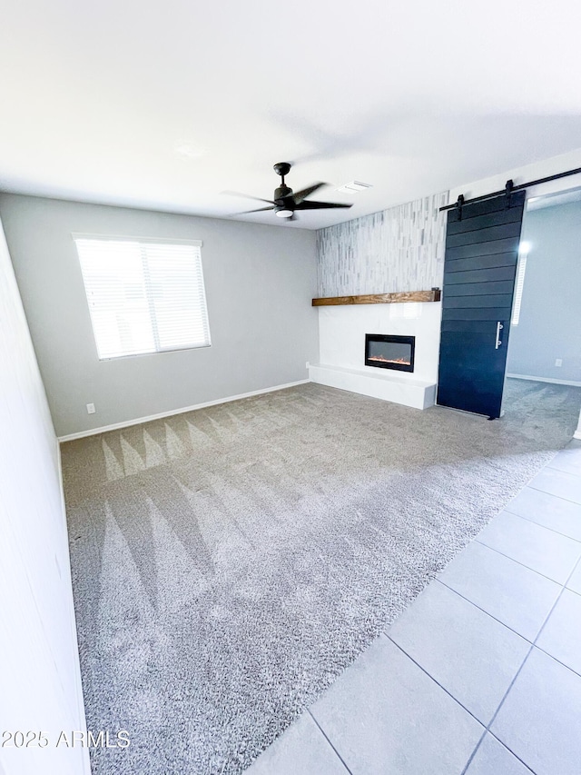 unfurnished living room featuring baseboards, carpet floors, ceiling fan, a glass covered fireplace, and a barn door