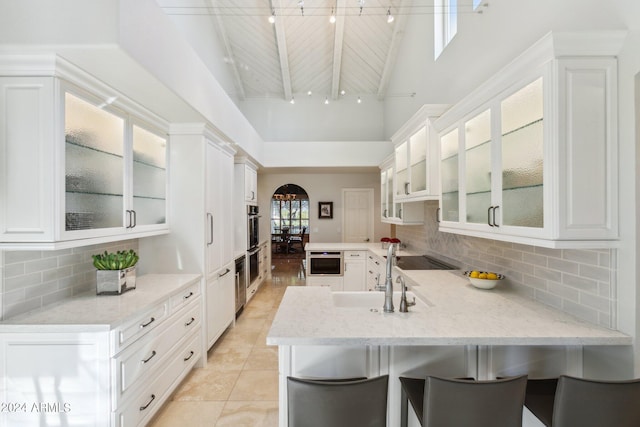 kitchen featuring kitchen peninsula, a kitchen breakfast bar, sink, high vaulted ceiling, and white cabinetry