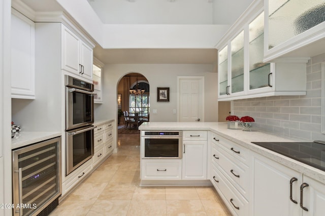 kitchen featuring backsplash, white cabinets, wine cooler, double oven, and kitchen peninsula