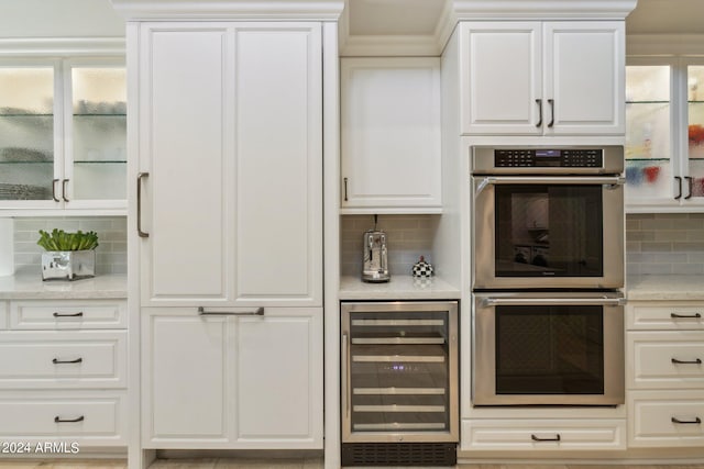 kitchen featuring double oven, decorative backsplash, white cabinetry, and beverage cooler