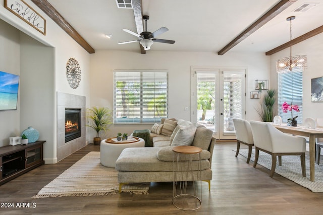 living room with ceiling fan with notable chandelier, beam ceiling, a tile fireplace, and dark hardwood / wood-style floors