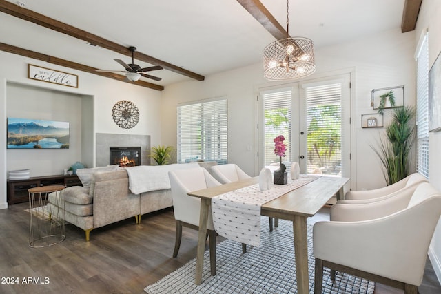 dining room featuring dark wood-type flooring, ceiling fan with notable chandelier, a tiled fireplace, beamed ceiling, and french doors