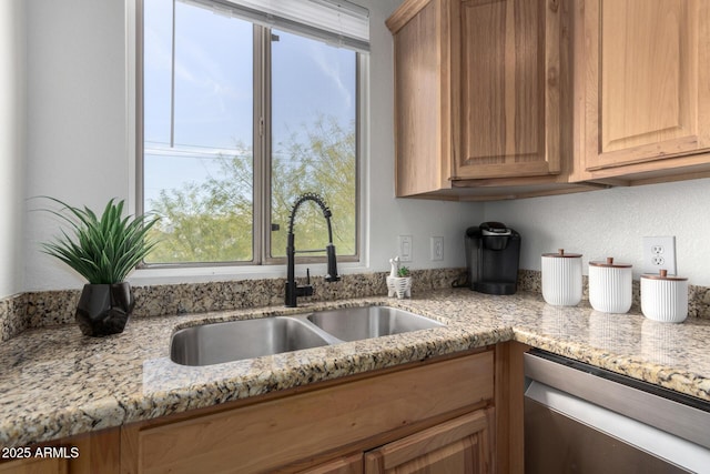 kitchen with stainless steel dishwasher, light stone countertops, and sink