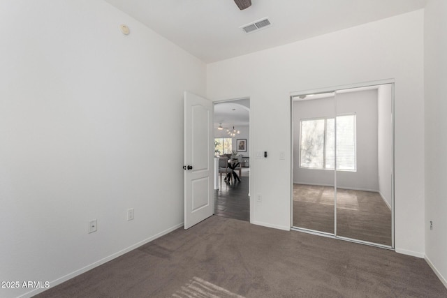 unfurnished bedroom with an inviting chandelier, dark carpet, and a closet