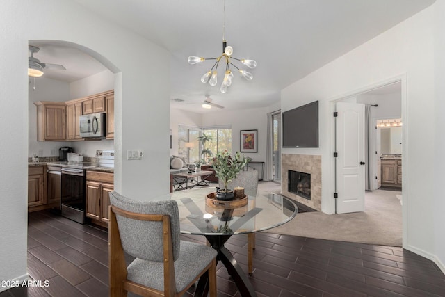 dining space featuring ceiling fan with notable chandelier and a tile fireplace