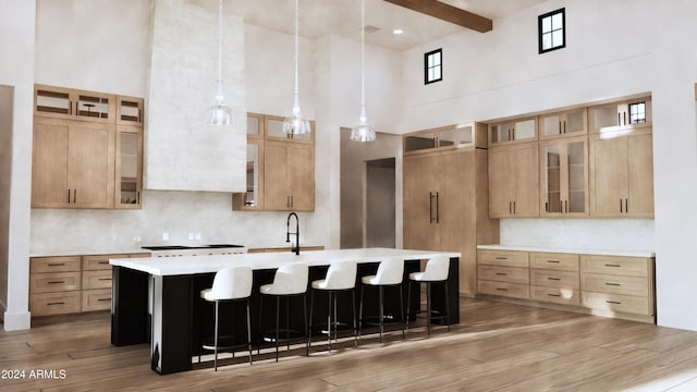 kitchen with light hardwood / wood-style flooring, beamed ceiling, a high ceiling, hanging light fixtures, and an island with sink