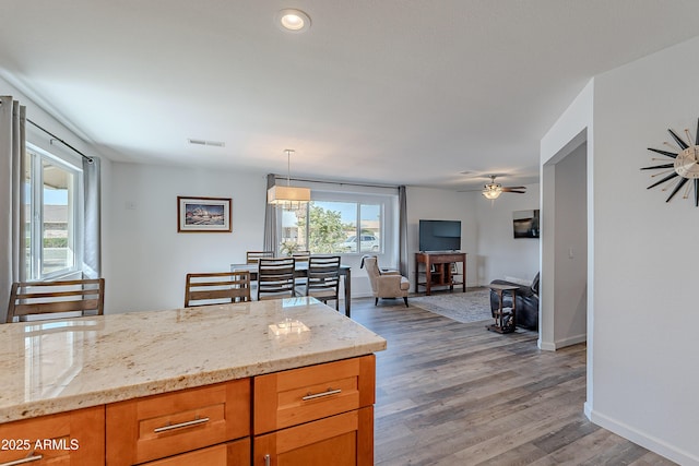 kitchen featuring light stone counters, ceiling fan, decorative light fixtures, and hardwood / wood-style flooring